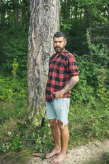 Bearded hipster in woods. Brutal lumberjack waiting on path. Barefoot guy standing on ground