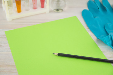 record diagnosis, medical report: the green sheet of blank paper and black pencil on it, around in selective focus, test tube, flask, gloves of a medical expert, in perspective