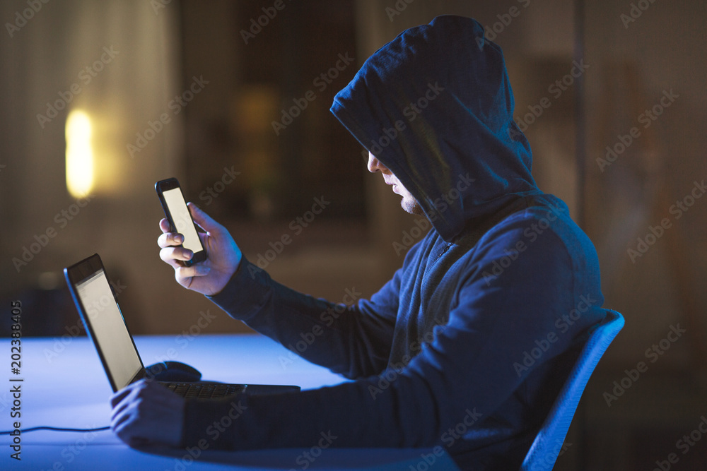 Aufkleber cybercrime, hacking and technology concept - male hacker with laptop computer and smartphone in dark