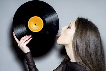 Sexy woman lick vintage vinyl disc. Woman with makeup face hold vinyl record. Fashion girl with long brunette hair. Music sound and entertainment concept
