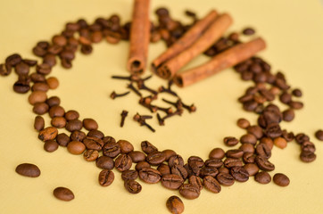 three sticks of cinnamon in a circle of coffee beans and clove spice on a yellow background