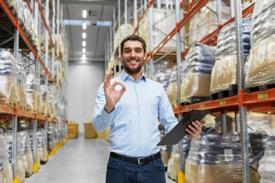 wholesale, logistic, business, export and people concept - happy man or manager with clipboard at warehouse showing ok hand sign