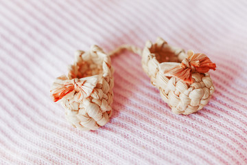 Cute tiny sandals made of straw, ancient traditional russian type of footwear. Natural booties for baby girl with a bow on pink knitted fabric background.