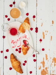 Top view of fresh croissants served with ripe raspberries and raspberry jam on white plate with lettering Bonjour over wooden background © PINKASEVICH