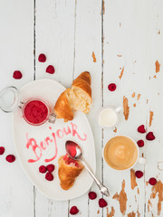 Top view of fresh croissants served with ripe raspberries and raspberry jam on white plate with lettering Bonjour over wooden background © PINKASEVICH