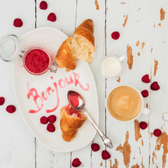 Top view of fresh croissants served with ripe raspberries and raspberry jam on white plate with lettering Bonjour over wooden background © PINKASEVICH