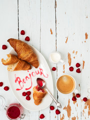 Top view of fresh croissants served with ripe raspberries and raspberry jam on white plate with lettering Bonjour over wooden background © PINKASEVICH