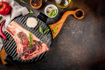 Raw beef marbled meat striplon rib eye steak with spices, grill pan, and herbs, dark background top view, copy space
