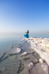 Fototapeta na wymiar Blonde young girl in a blue dress on the shore of the dead sea. Jordan