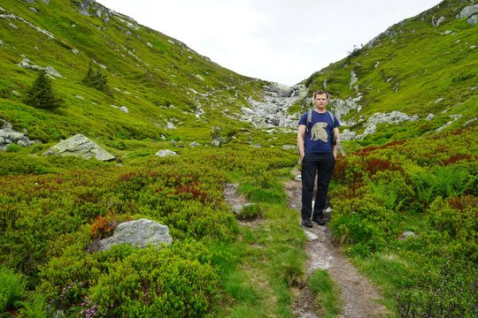 View mountains and a tourist standing on a footpath.