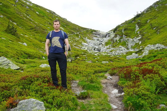 A man with backpack standing on background of small mountains.