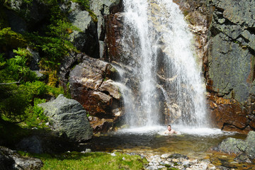Man in mountains takes shower under cold waterfall.