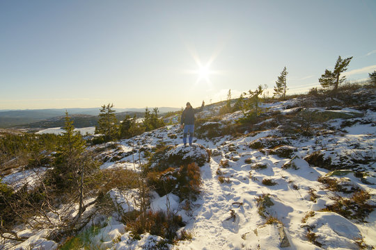 A man standing on the mountain area and pointing to the sun.