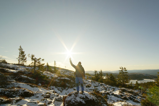 A man standing on the mountain area and pointing to the sun.