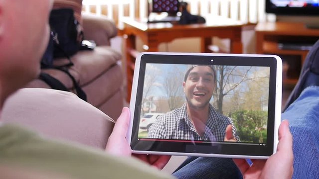 A man in his living room watches a popular vlogger playing on his tablet PC.  	