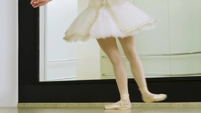 Close-up shot of feet of female ballet dancer dancing on tiptoe in pointe shoes in dance studio. 4K