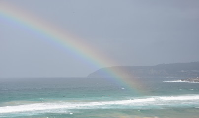 Rainbow over the Tasman sea. Seascape with beautiful multicoloured rainbow over the sea and Curl Curl beach, Australia. Surfers in the water.