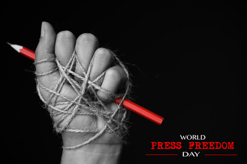 Hand with red pencil tied with rope, depicting the idea of freedom of the press or freedom of...