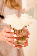 Female hands with beautiful manicure hold in hands a small vase with white roses