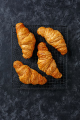 Croissants on a cooling rack on textured dark background, top view. Copy space.