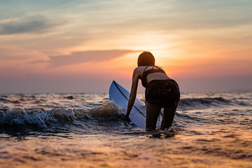 slim woman going to suftboard in the sea at sunset