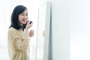 Asian woman applying make up in front of a mirror.