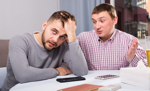 Friend calming distressed guy at home table