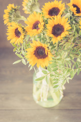 Bouquet of bright sunflowers in a glass jar on a wooden table. Retro toned.