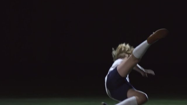 Tilt up of junior soccer player shooting a ball and falling down on artificial turf in indoor arena in low key lightning
