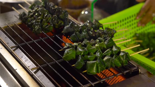 Process of making a barbecue of a minced meat wrapped in a palm leaves on a night market in Thailand. Thai food concept. Asian food concept