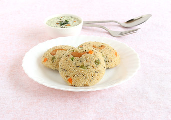 Oats Idli or cake, a healthy Indian vegetarian food, with vegetables like carrot, peas, green beans and capsicum, and cashew nuts, which is steam cooked, and coconut chutney.