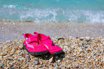 Coral slippers. Summer girl shoes for stones beach.Pink water shoes. Shoes which protect foot on a beach.Summer vacation background with a pair of sandals on beach.Copy space