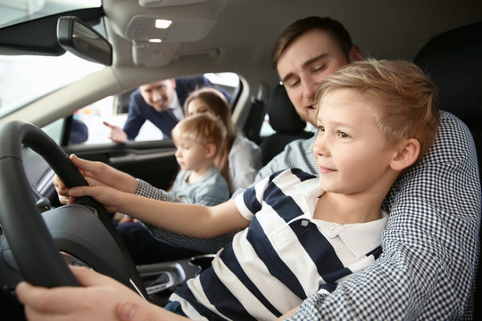 Young Family Choosing New Car With Salesman In Salon