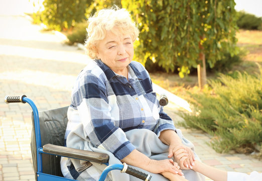 Senior woman in wheelchair holding hands of nurse from care home outdoors