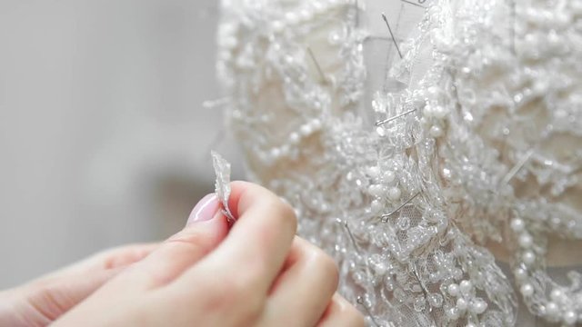 Close-up fashion designer for brides in his Studio pins needles lace wedding dress. Seamstress creates an exclusive wedding dress. Secure with pins and needles outline. Small private business. Sew