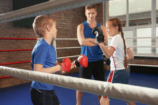 Little children with trainer on boxing ring