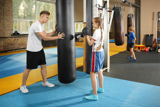 Little girl with trainer near punchbag in gym