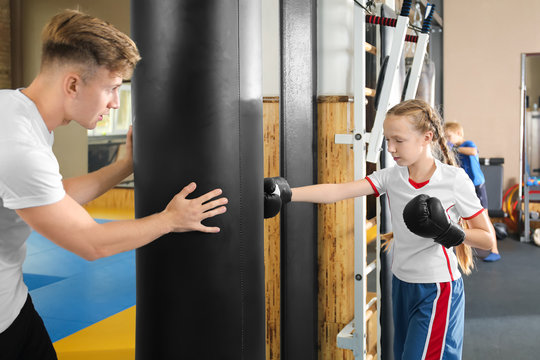 Little girl with trainer near punchbag in gym