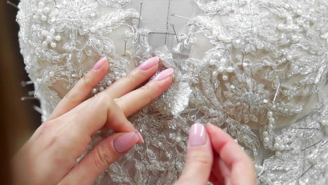 Close-up fashion designer for brides in his Studio pins needles lace wedding dress. Seamstress creates an exclusive wedding dress. Secure with pins and needles outline. Small private business. Sew