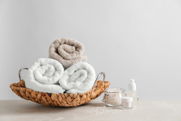 Basket with clean towels and cosmetic products on table against light background