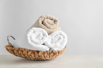 Basket with clean towels on table against light background