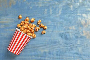 Delicious popcorn with caramel in paper bucket on wooden background, top view