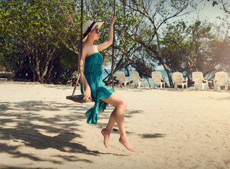 Girl swinging on a swing. A girl in a hat and a dress. Beach vacation.