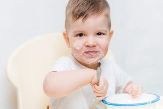 adorable baby boy eats porridge with a small spoon himself
