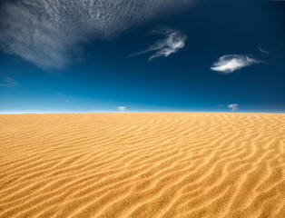 Fototapeta na wymiar Textured sand surface, dark blue sky with clouds