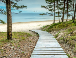 Fototapeta na wymiar Wooden footpath is leading to the sandy beach of the Baltic Sea. In the Baltic countries tourism is mostly targeted at a human health maintenance . 