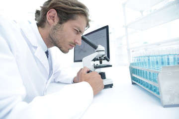Young laboratory scientist looking at microscope in laboratory