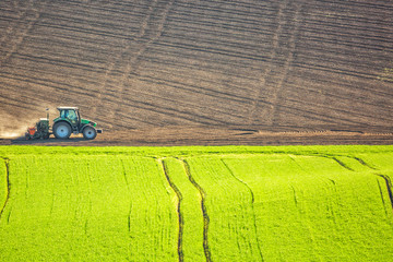 Fototapeta na wymiar Beautiful spring landscape with working tractor on green and brown field in South Moravia, Czech Republic. Agriculture concept.