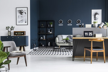 Spacious living room interior with sofa, shelf, retro armchair, blue cabinet and workplace corner...