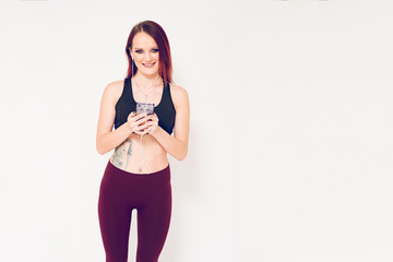 fitness girl brunette holding a smartphone on a white background and smiling
